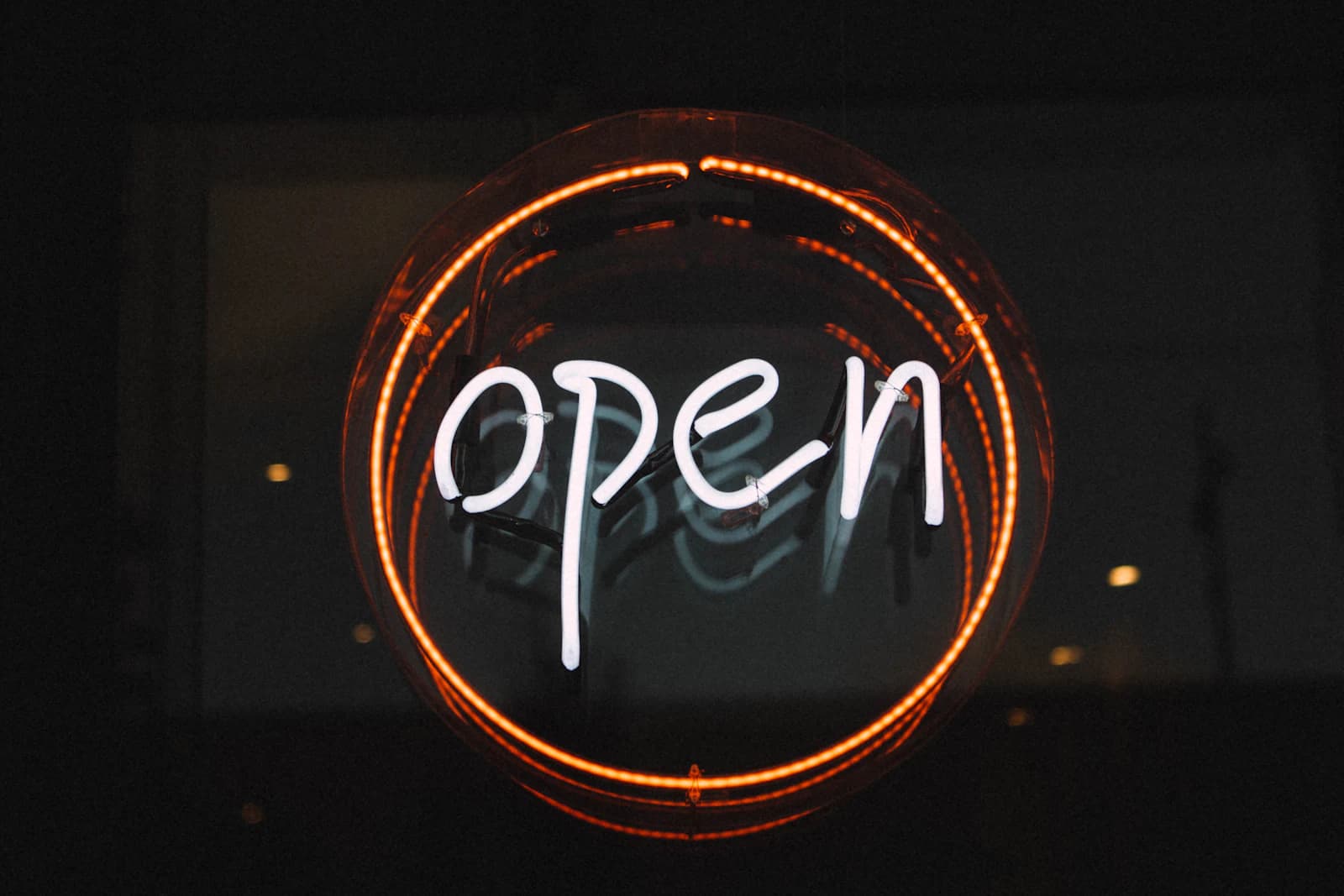 Round neon 'open' sign glowing in a dark shop window